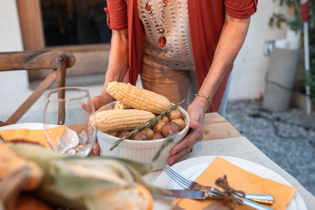 Woman placing corn and potatoes on a table set for dinner