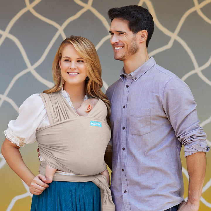 mom wearing baby in elements wrap in taupe with man next to mom