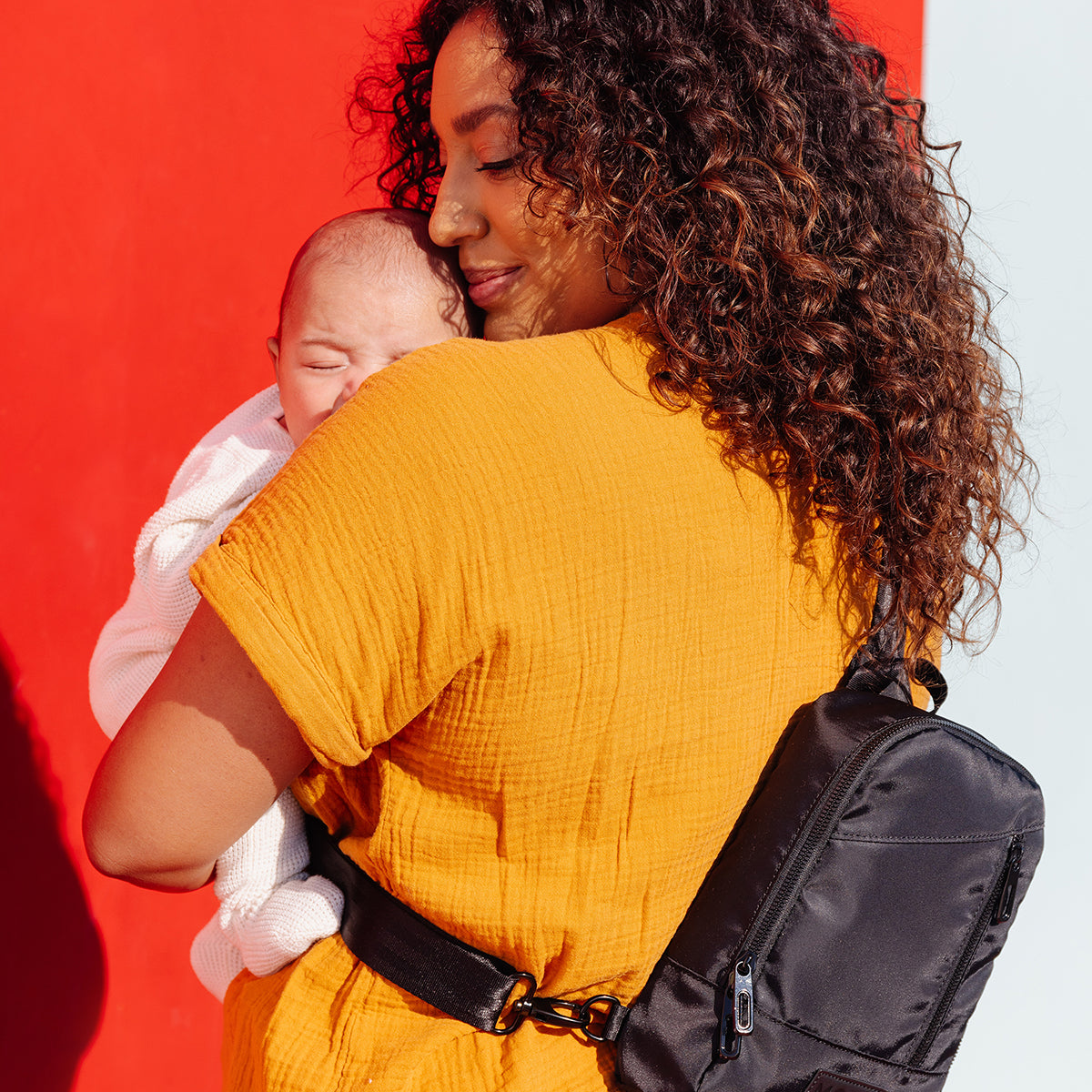 mom wearing the transit cross body in black while hugging baby