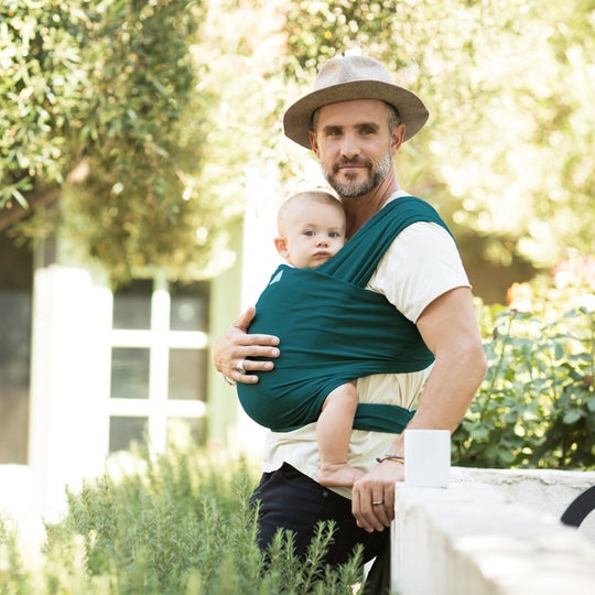 Dad wearing hat and carrying baby in a moby wrap