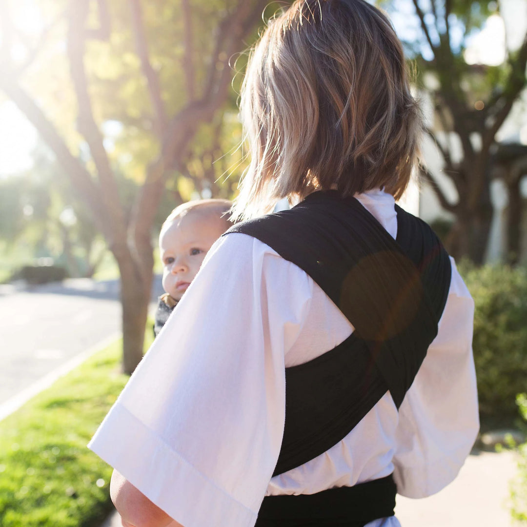 moby wrap shown from back of female caregiver displays wide stretchy fabric straps designed to distribute weight comfortably