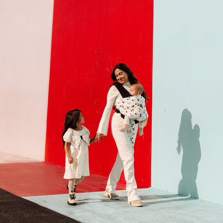 mom wearing baby in Easy-Wrap Carrier in Disney's Mickey Mouse & Minnie Mouse while walking and holding hands with toddler girl