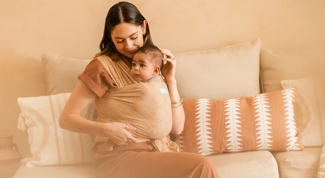 mom sitting on couch and wearing baby in classic wrap in sand waves