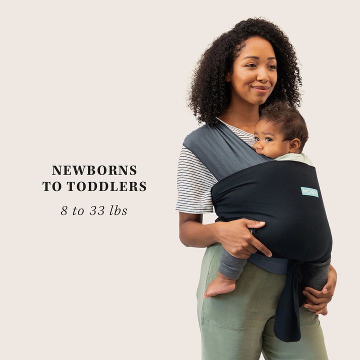 mom wearing easy-wrap baby carrier in charcoal/black color. demonstrating use from newborns to toddlers 8 to 33 lbs