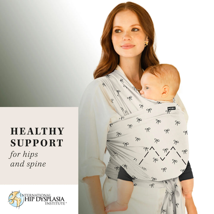 mom wearing baby in Classic Wrap Baby Carrier in Belles & Bows. healthy support for hips and spine by international hip dyslpasia institute.