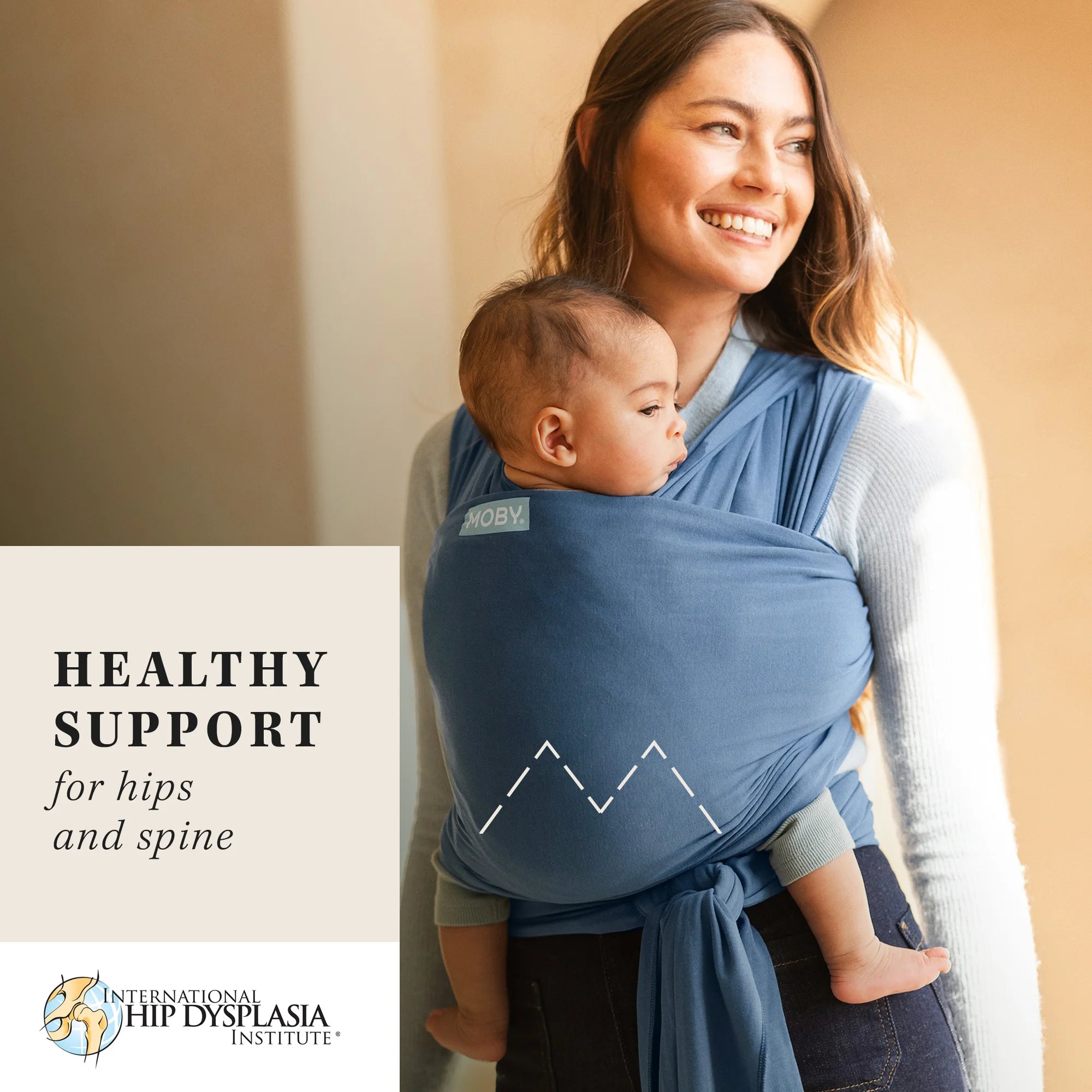 mom wearing baby in classic wrap in ocean. healthy support for hips and spine from the international hip dysplasia institute.