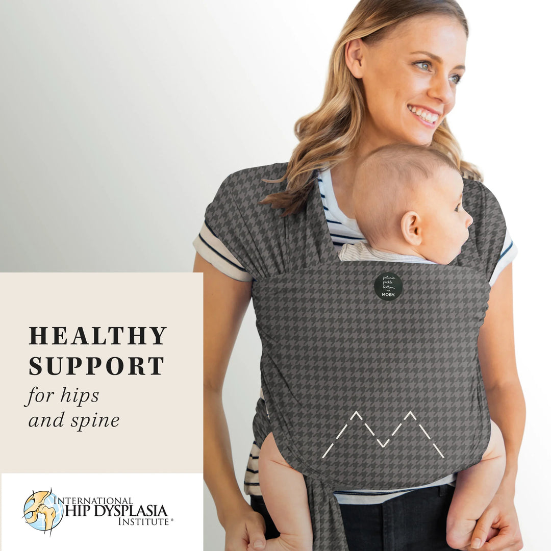 mom wearing baby in Classic Wrap Baby Carrier by Petunia Pickle Bottom in Houndstooth. healthy support for hips and spine by international hip dysplasia institute