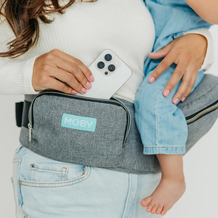 mom wearing baby in hip seat in heather grey while putting in iphone in pocket