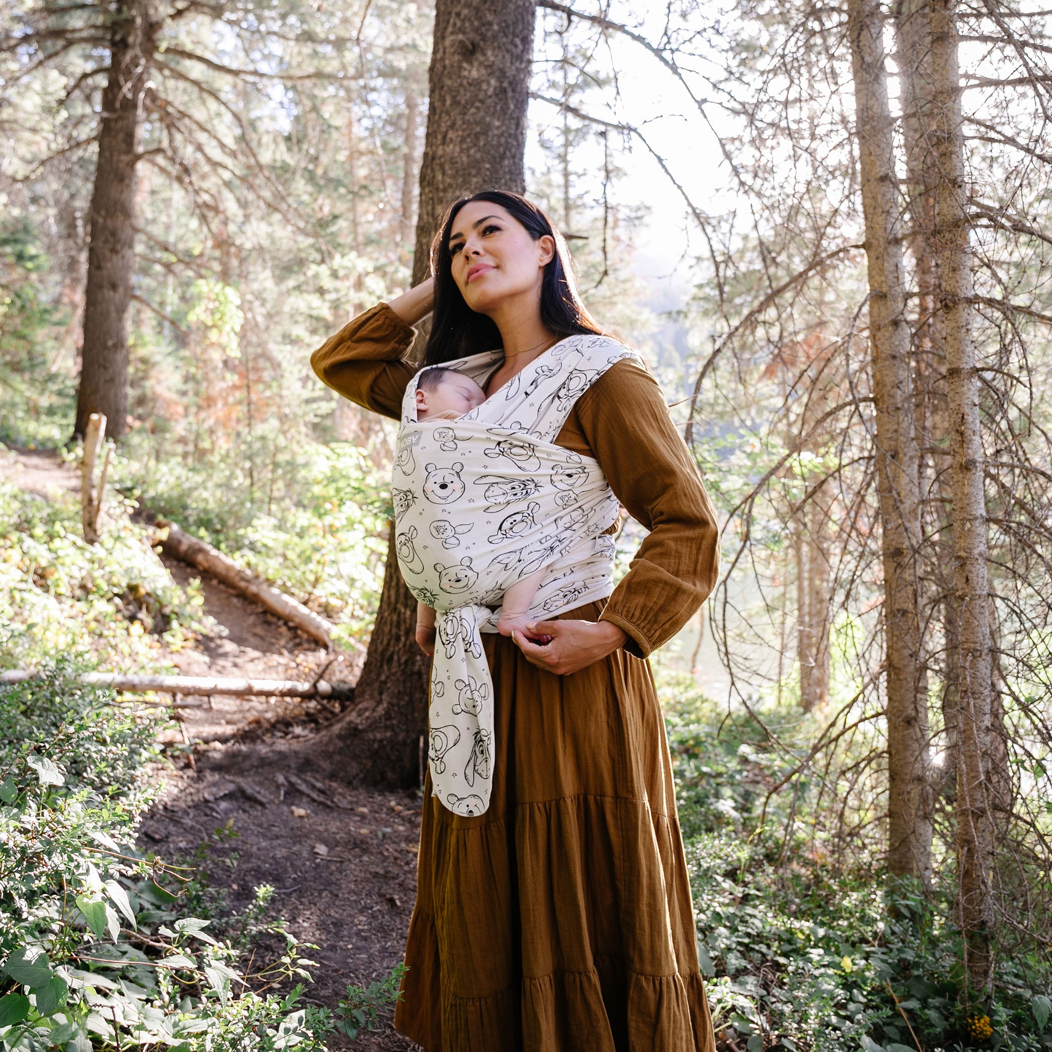 mom standing in woods wearing baby in featherknit wrap in winnie the pooh and pals