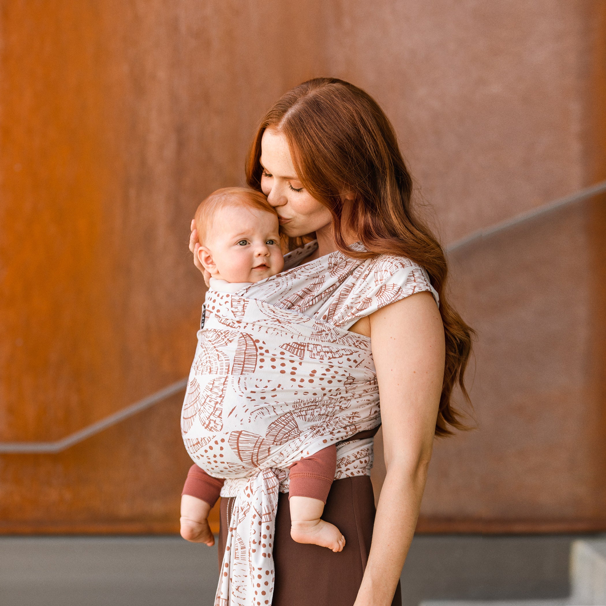 mom wearing baby in petunia and moby evolution wrap in woodgrain