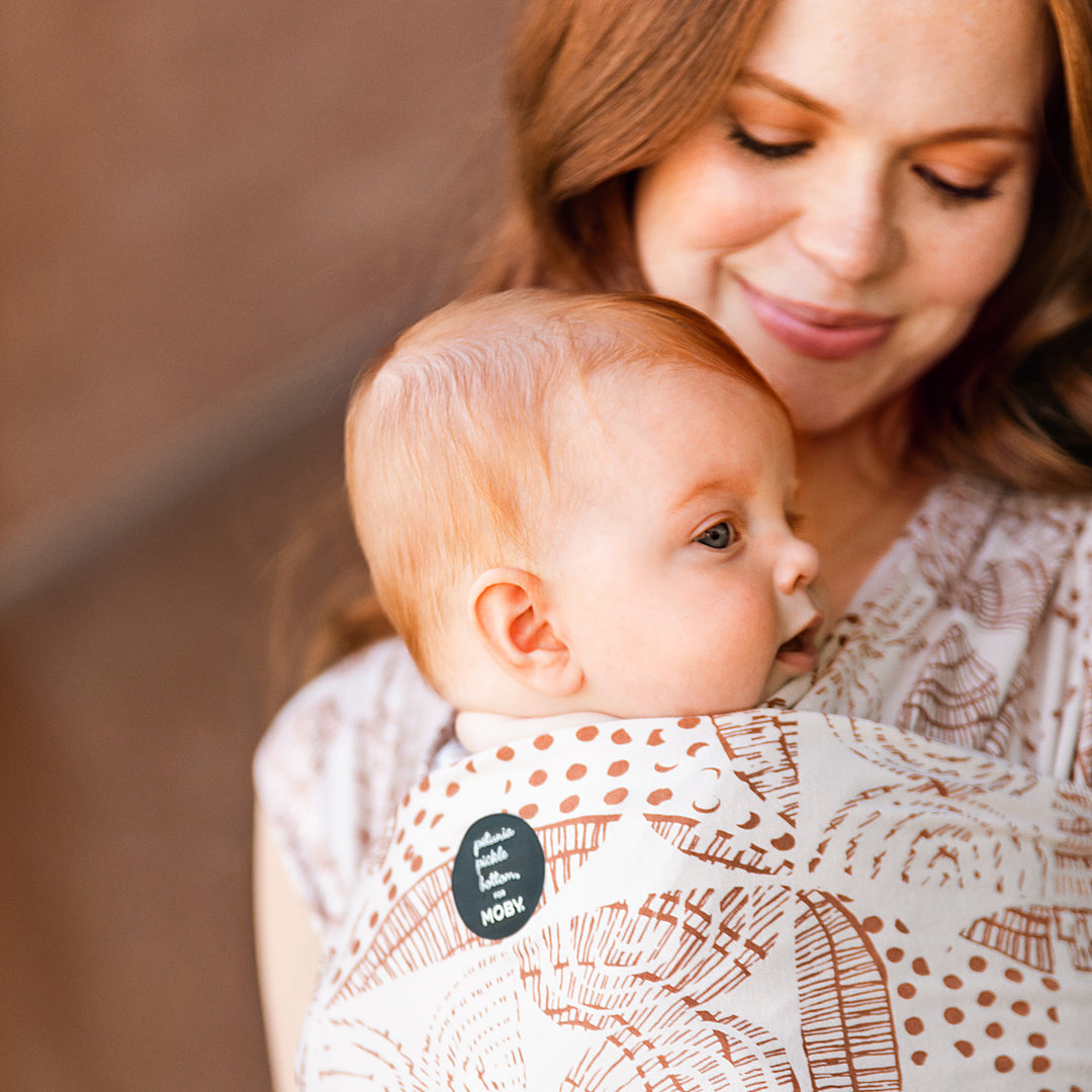 mom wearing baby in petunia and moby evolution wrap in woodgrain